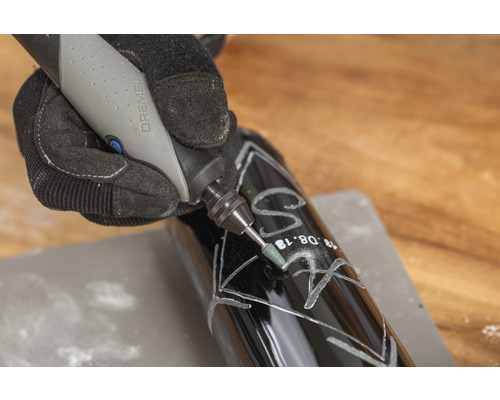 En person graverar en mörk flaska med ett Dremel verktyg.
