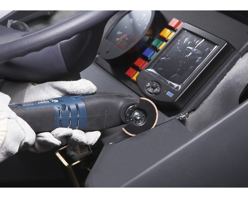 Operatör med skyddshandskar använder ett multifunktionsverktyg för att skära ett material på en byggarbetsplats