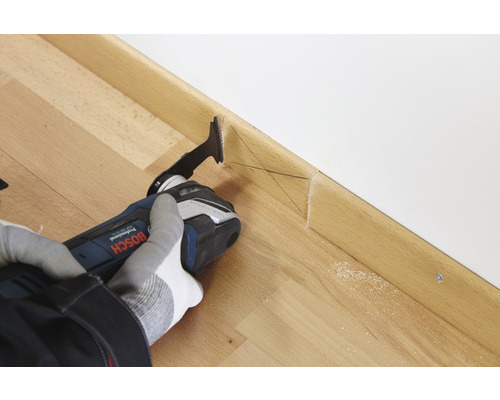 En person skär en golvsockel i trä med ett multiverktyg.