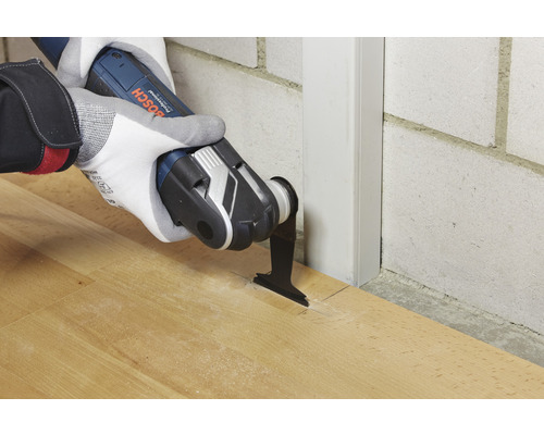 Oscillerande multiverktyg i bruk på trägolv bredvid en vägglist.