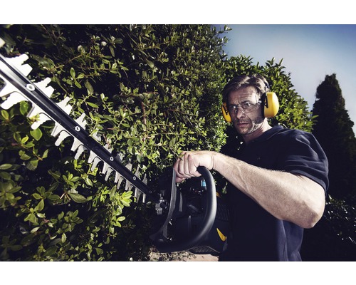 Man klipper häck med en häcksax, bär hörselskydd och skyddsglasögon.