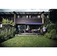 En man klipper en häck med en häcksax i en trädgård framför ett hus.