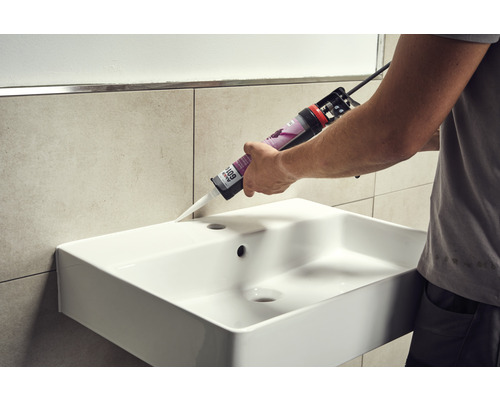 En hantverkare tätar ett handfat med silikon.