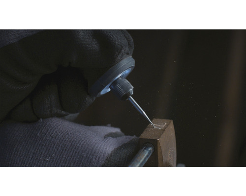 Närbild av en hand med skyddshandske som graverar en form i ett metallföremål med en gravyrstickel