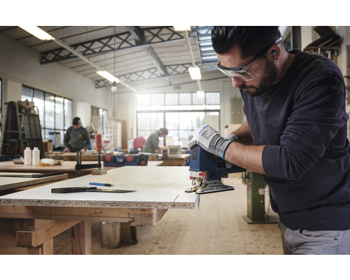 En man sågar ett arbetsstycke med en sticksåg i en verkstad.