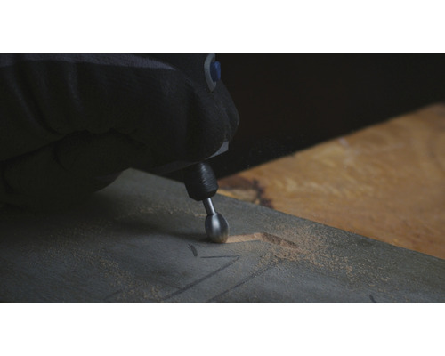 En person graverar ett mönster i en träbräda med ett multifunktionsverktyg.