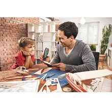 Far och son bygger tillsammans en modellflygplan med en limpistol vid ett bord.