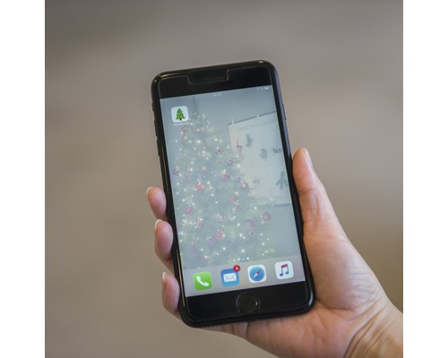 En mobiltelefon hålls och visar Hornbach-appen med en julgran i bakgrunden.