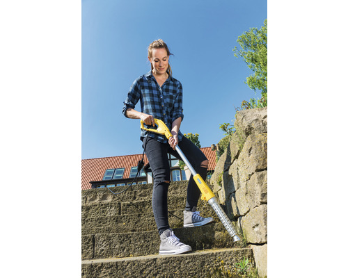 En kvinna tar bort ogräs med en elektrisk ogräsrensare på en stentrappa.