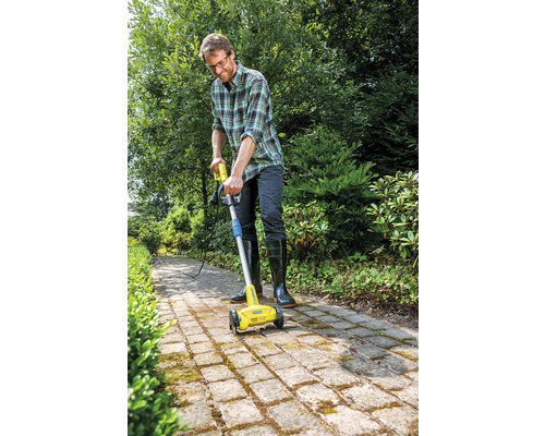 En man använder en elektrisk fogborste för att rengöra en stenlagd gång i trädgården.