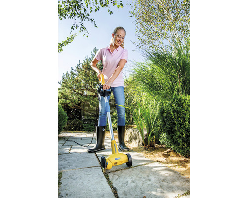 En kvinna använder en elektrisk fogrensare för att ta bort ogräs mellan stenplattor.