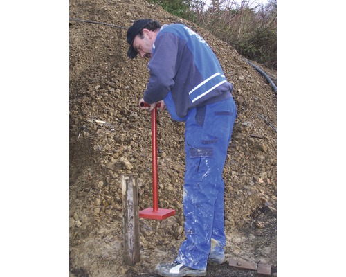 En man slår ner en trästolpe i marken med en markstöt.