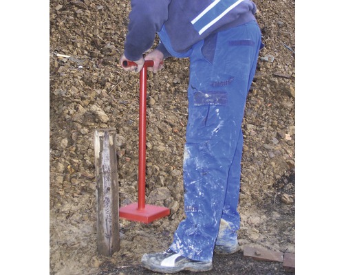 En person slår ner en trästolpe i marken med en markstamp.