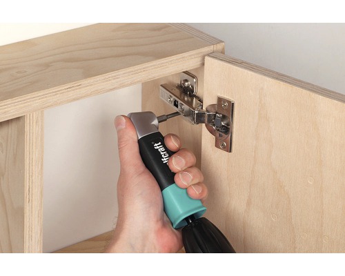 En person fäster ett möbelskåpsgångjärn på ett träskåp med en vinkelskruvdragare.