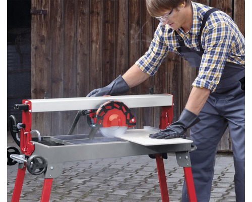 En man med skyddsglasögon och handskar använder en kakelskärare för att skära en kakelplatta.