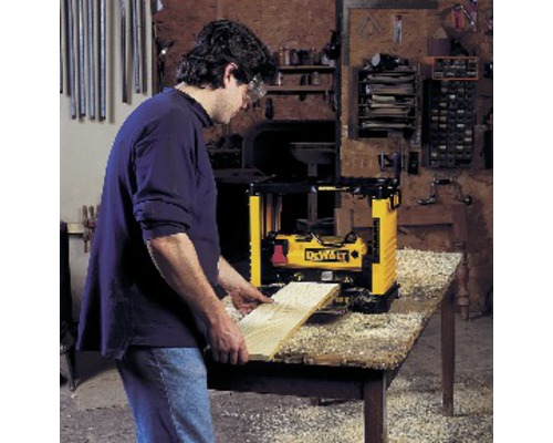 En man hyvlar en träplanka med en DeWalt hyvel på ett bord.