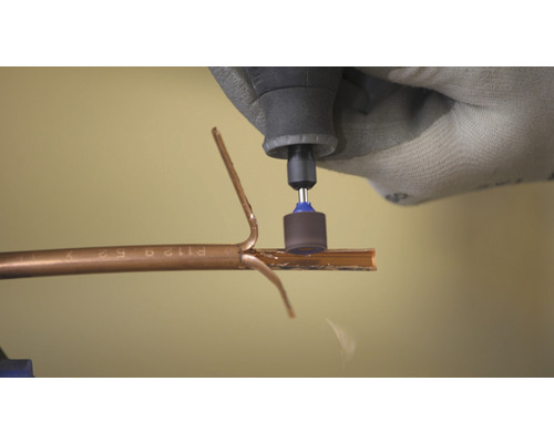 En person använder ett multifunktionsverktyg för att skära ett rör.