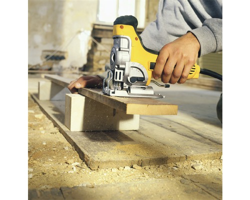 Person sågar träbräda med sticksåg. Brädan ligger på ett block.