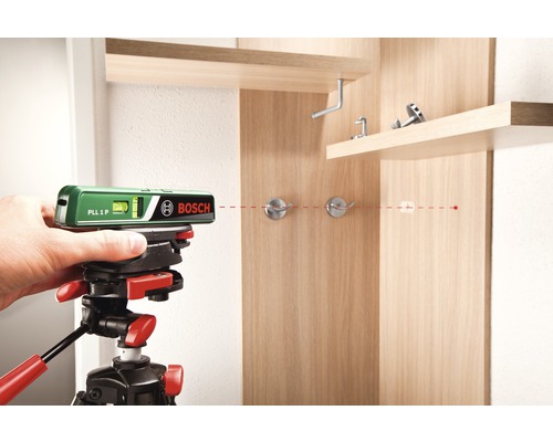 Bosch logotyp. Korslinjelaser på stativ projicerar en röd linje på en träskåpsvägg.