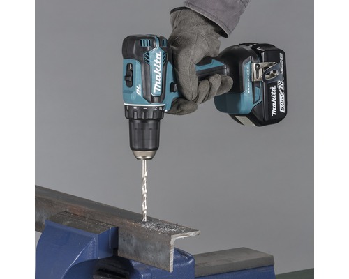 Makita sladdlös skruvdragare som borrar genom en metallbit som sitter fast i ett skruvstäd.