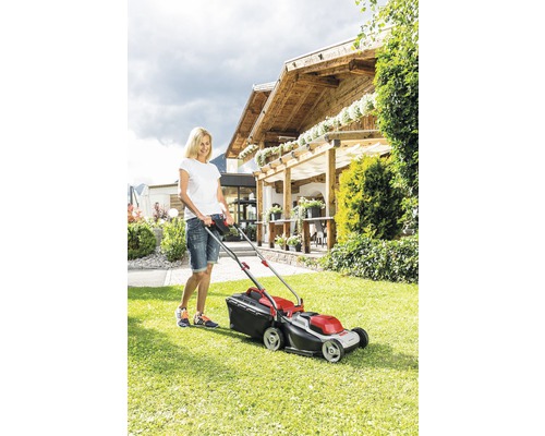 Kvinna använder gräsklippare i trädgården