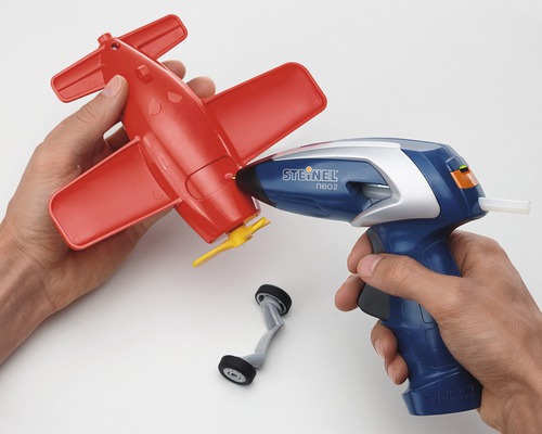 Person som limmar ihop ett rött leksaksflygplan med limpistol