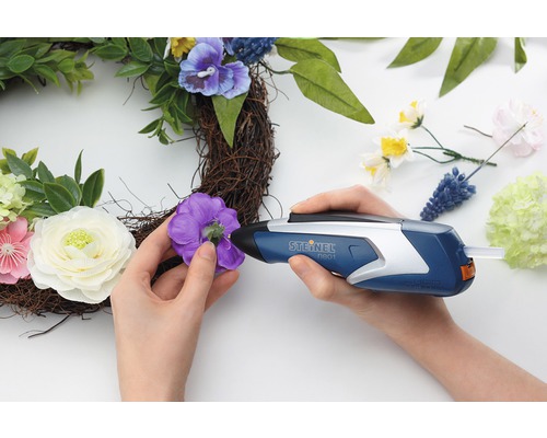 Person fäster en blomma på en krans med en limpistol.