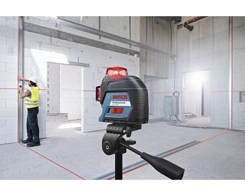 Bosch logotyp. Byggarbetsplats med krysslaser på stativ, som projicerar röda laserlinjer på väggar och golv. Arbetare med skyddshjälm och varselväst riktar in en metallskena.