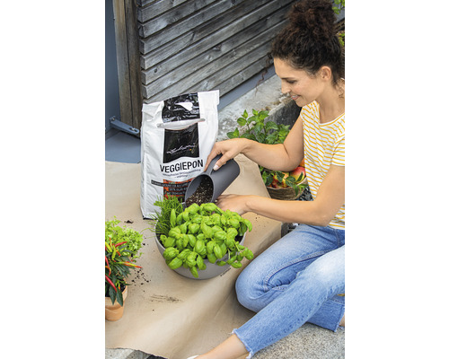 Kvinna fyller en blomkruka med örter och Veggiepon grönsaksjord.