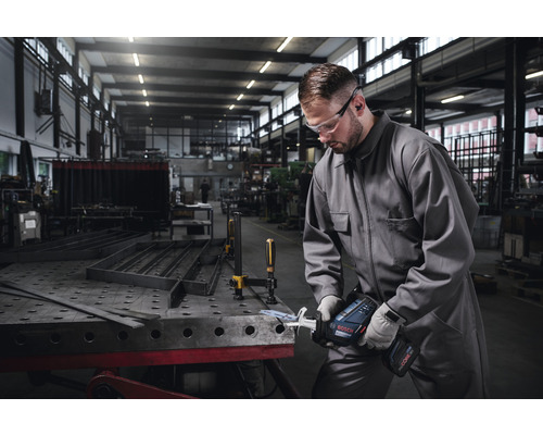 Man med skyddsglasögon och hörselskydd arbetar med en batteridriven tigersåg på en metalldel i en verkstad.
