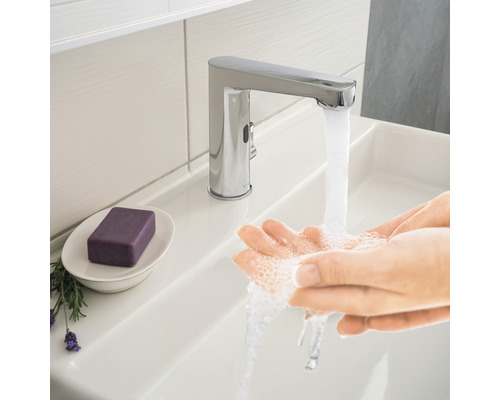 Person som tvättar händerna under en förkromad kran i tvättställ.