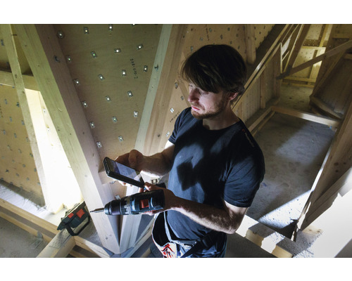 Man fotograferar med en mobiltelefon en borrmaskin framför en takstol av trä