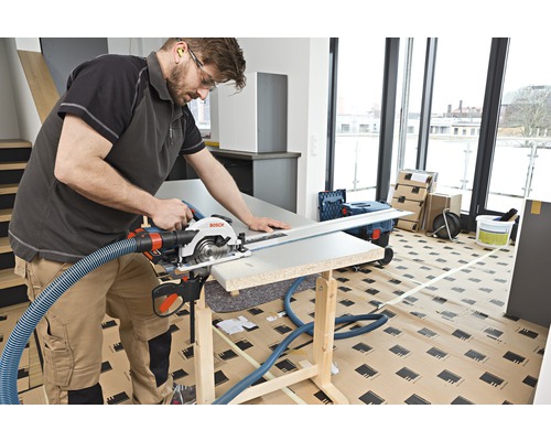 Hantverkare sågar ett arbetsstycke med en cirkelsåg på en arbetsbänk. En sugslang är fäst vid sågen.