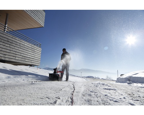 En person använder en snöslunga på en snöig väg.