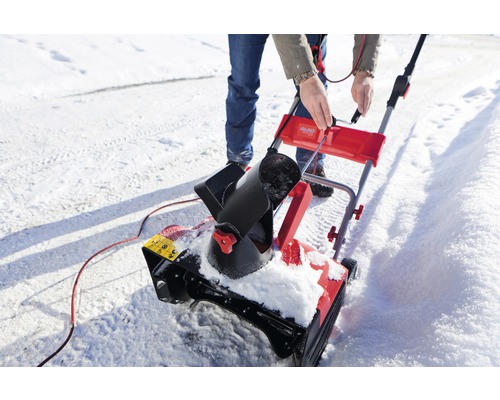 En person använder en snöslunga på en snöig yta.