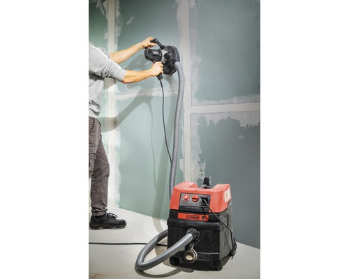 Man slipar en vägg med en gipsskiveslipmaskin ansluten till en dammsugare.