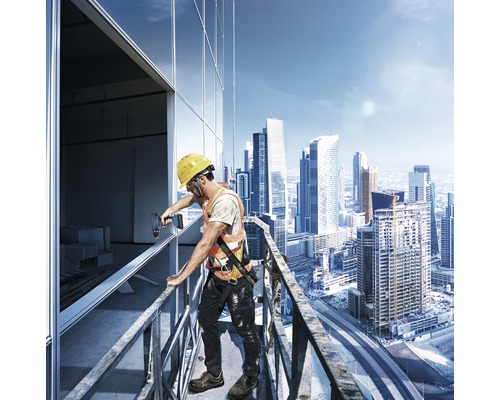 En byggnadsarbetare med hjälm och säkerhetsväst monterar fönster på en byggnad på hög höjd