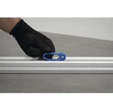 En hand med skyddshandske fäster en blå skjutreglage på en aluminiumskena.