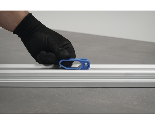 En hand med skyddshandske fäster en blå skjutreglage på en aluminiumskena.