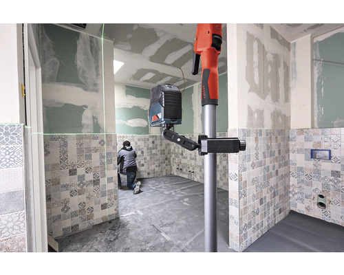 En arbetare använder ett linjelaserinstrument med stativ i ett badrum med kakel.