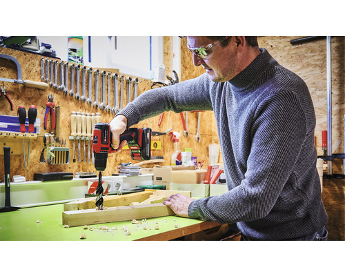 Man borrar ett hål i en träplanka med en batteridriven borrmaskin i en verkstad.