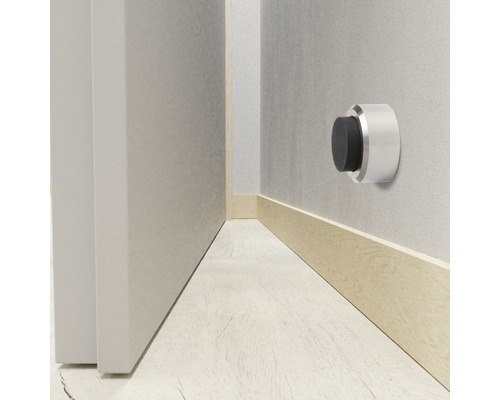 Väggmonterad dörrstopp av metall med gummibuffert bredvid en dörr