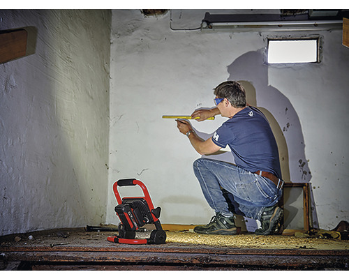 Man mäter vägg med tumstock, byggstrålkastare lyser upp rummet