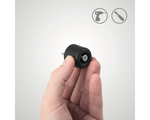 En hand håller en svart dörrstopp för montering med skruv. Installationssymboler i bakgrunden.