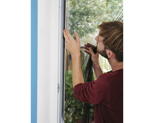 Man fäster ett myggnät på en fönsterkarm.