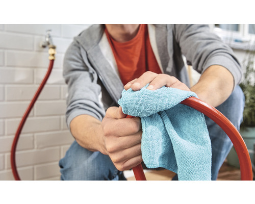 En person rengör en slang med en trasa i ett hus.