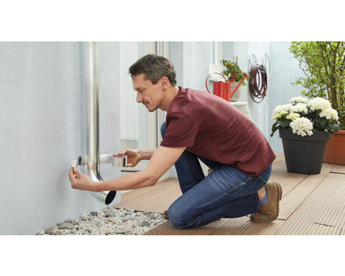 Man fäster ett stuprör på en husvägg med tätningsband.