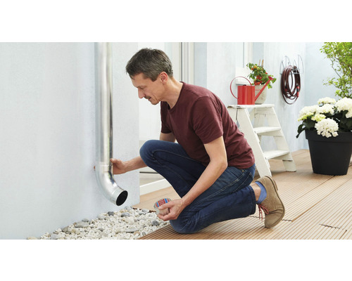 En man fäster ett stuprör på en yttervägg till ett hus.