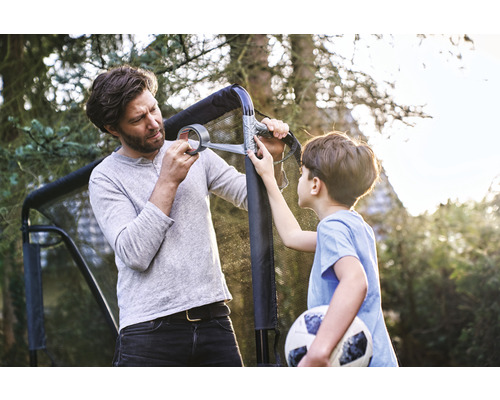 Far och son reparerar ett fotbollsmål med tejp i trädgården.