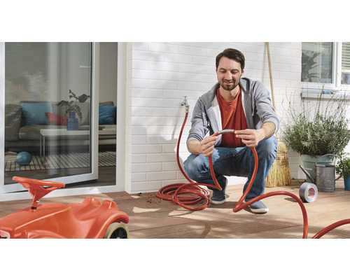 Man ansluter en trädgårdsslang till en vattenkran, med ett hus och en terrass i bakgrunden